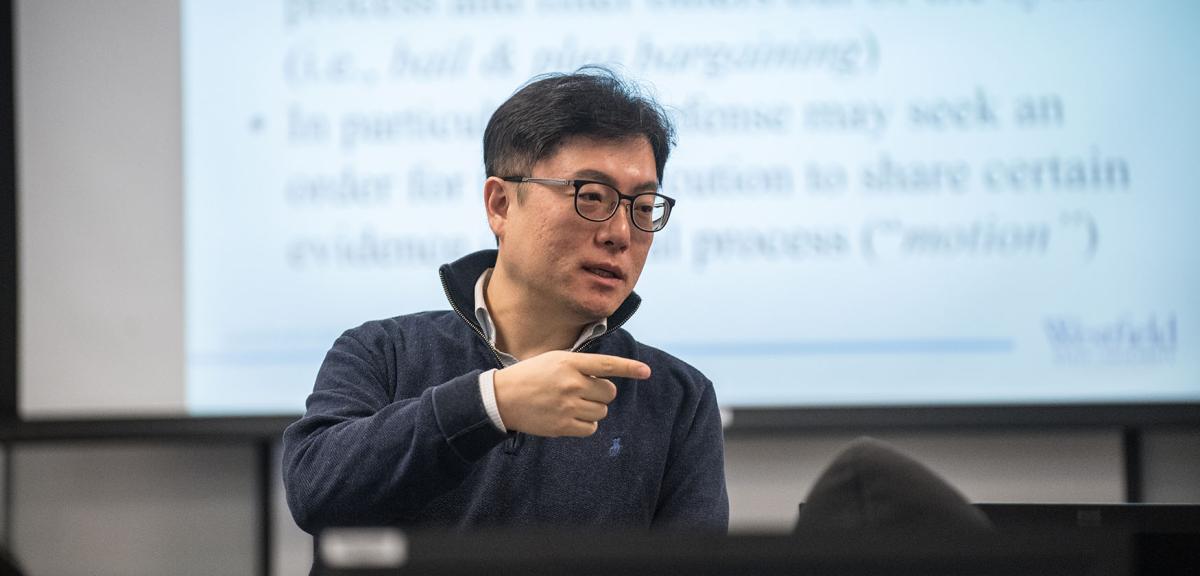 A Criminal Justice professor stands in front of a projection screen while instructing their class of students.