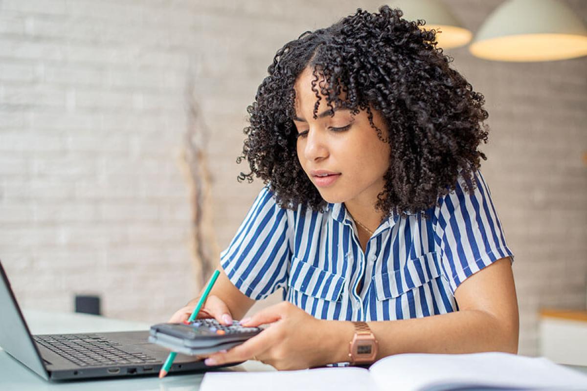 A person uses a calculator while working on a laptop.