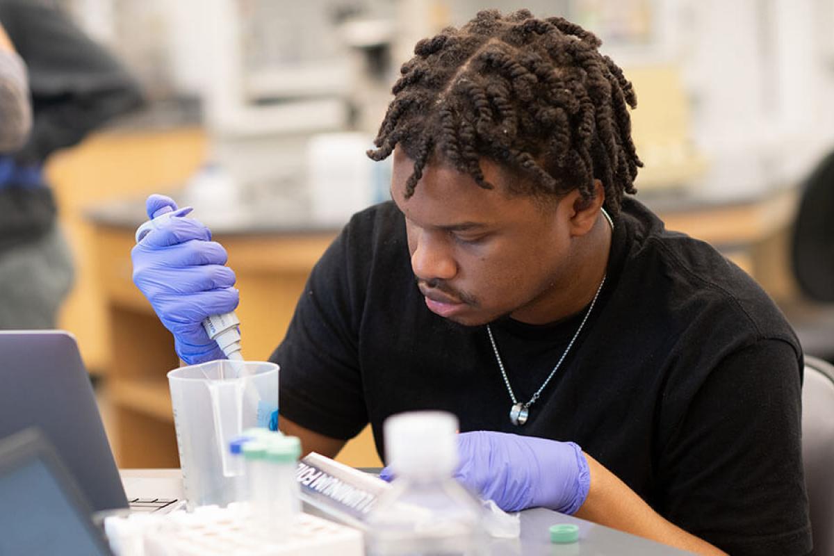 A student wearing rubber gloves conducts an experiment in a laboratory setting. 