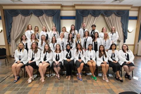 Graduating nursing students in their white coats pose for the camera.