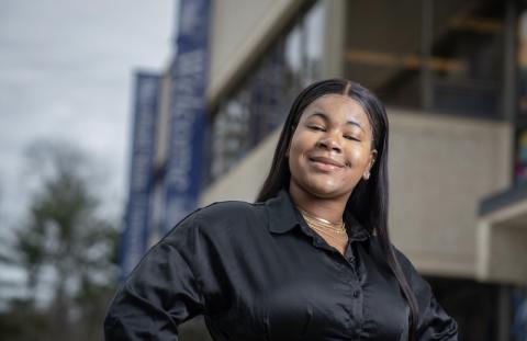 Ketia Valme, an English major and class of 2024, wears a black, long-sleeved shirt and smiles before the Ely center. 