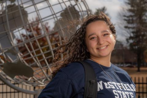 Stephanie Block, Class of 2025, a psychology major. She's posing in front of the campus globe and wearing a blue "Westfield State" shirt.