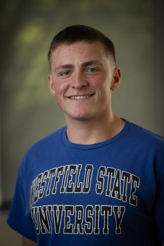 Matt Crusha ’27 smiles for a portrait while wearing a blue Westfield State University T-shirt.