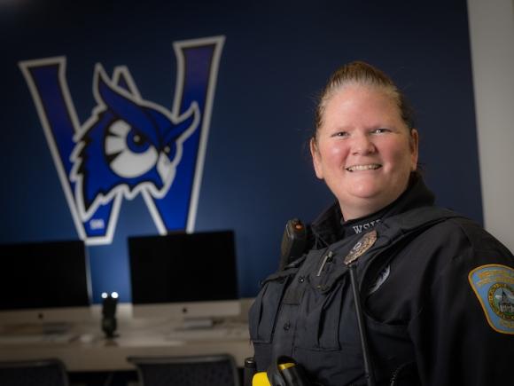 Officer McCue of Westfield State. She is wearing her police uniform and posing in front of a navy-blue Nestor mural.