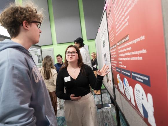 Accounting student presenting their research poster to another student.