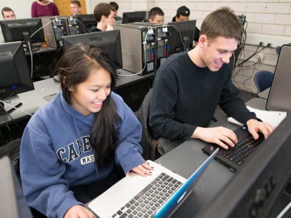 Two students smiling while working together in a computer in a lab.