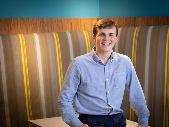 Student smiling sitting at a table with a striped background.