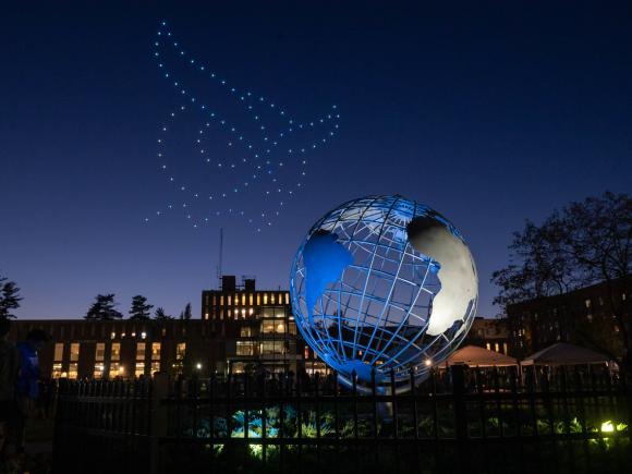 Drone show at Westfield State forming the Nestor logo in the night sky above the campus globe.