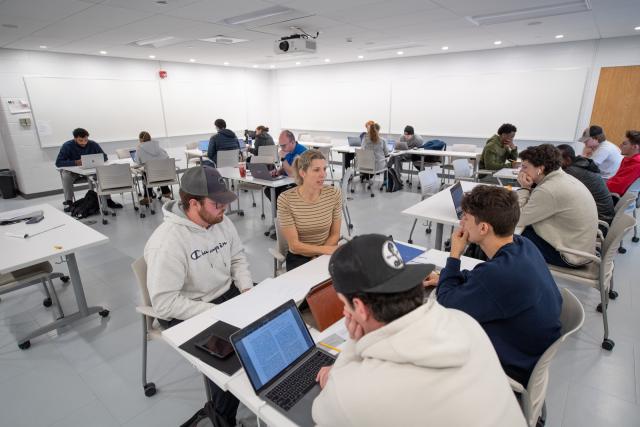 Economics class featuring instructor with small group of 3 students working on a project with laptops.