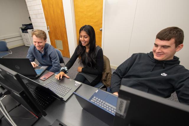 Three computer science students smiling in front of laptops.