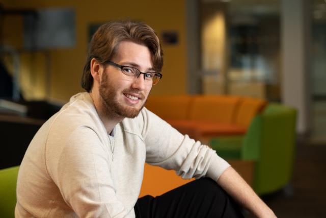 Education student in Parenzo Hall smiling wearing glasses and beige shirt.