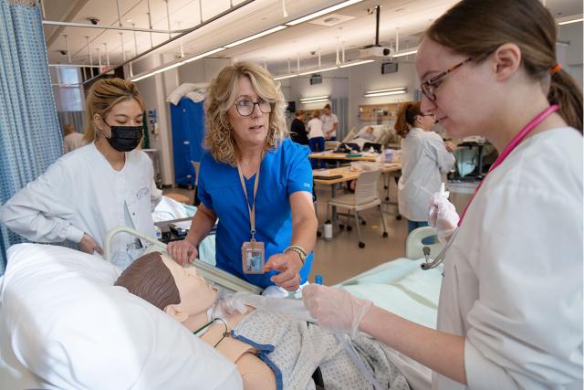 Two nursing students receive instruction from their professor while working hands-on in the simulation lab.