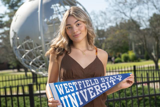 Student at campus globe holding a WSU pennant flag.