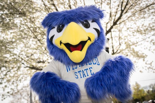 Nestor the owl mascot smiling with flowering trees.