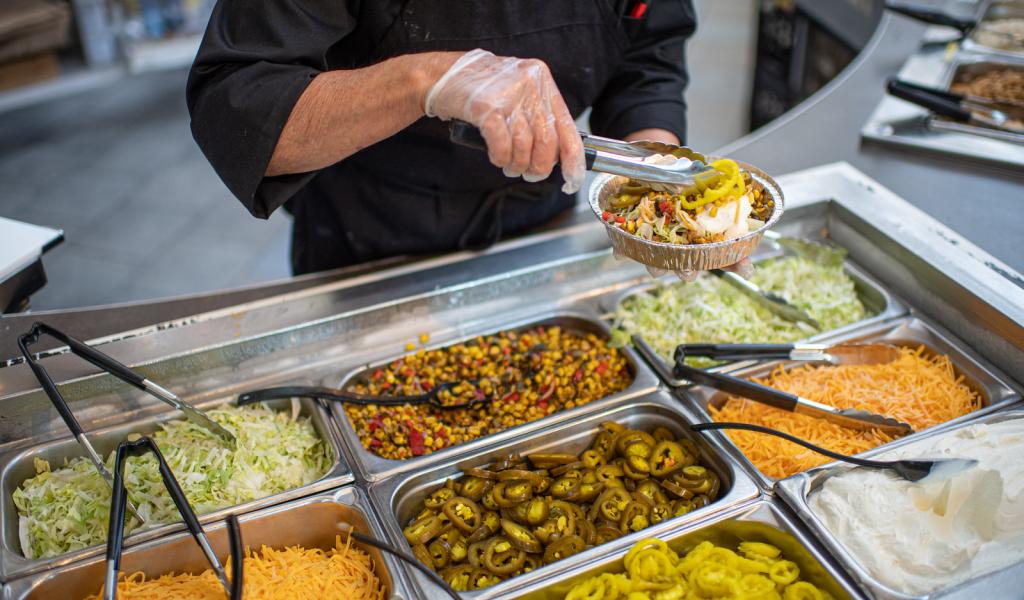 Dining services Mexican food station featuring lettuce, cheese, jalapenos, sour cream, and meat.