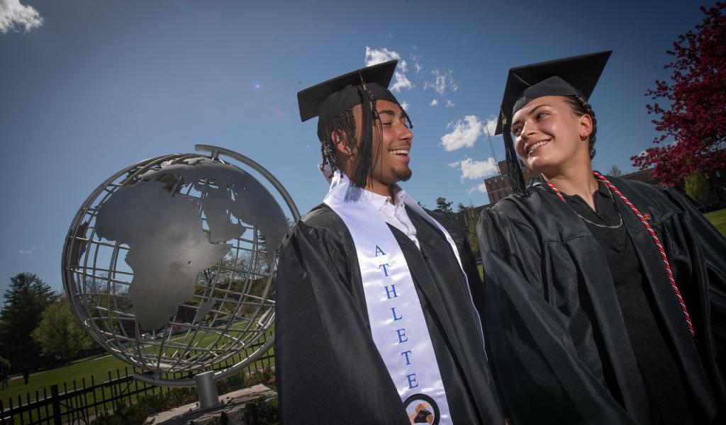 Two students wearing caps and gowns in front of campus globe.
