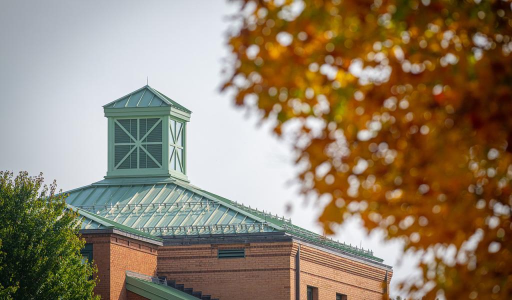 Courtney Hall in the fall with a tree in front of it with orange leaves.