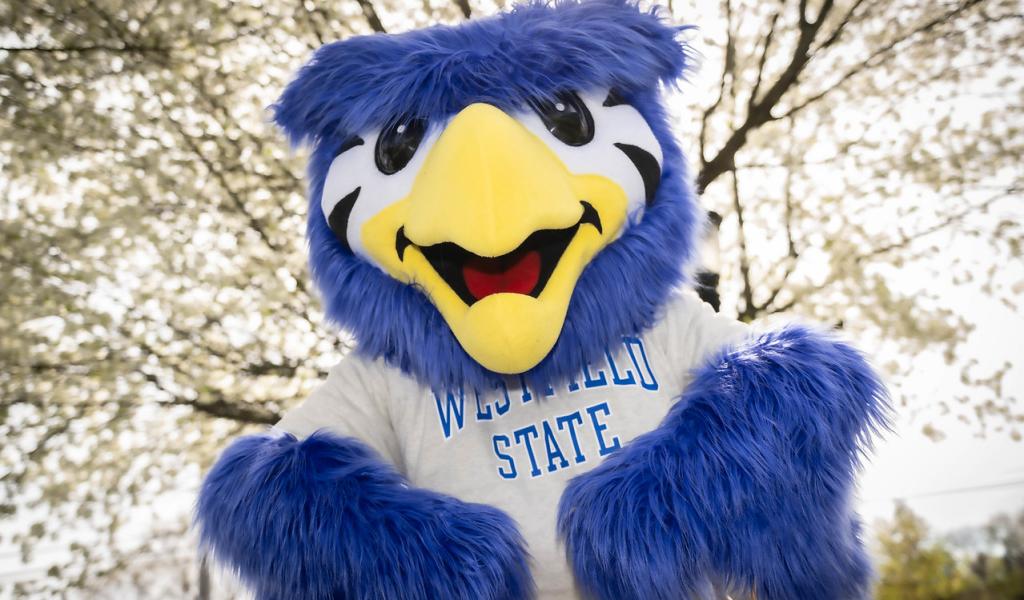Nestor the owl mascot smiling with flowering trees.