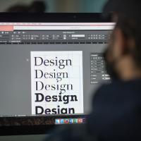 A stock photo of a student sitting in front of a computer, with him experimenting with typography in a graphic design class.