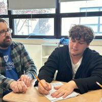 Westfield State alum and math teacher at Drury High School, Mark Brown. He is in a flannel and blue shirt as he helps one of his students in the classroom with the math lesson.