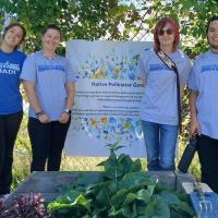 Four students stand in front of garden plants and a sign for Grandmothers' Garden